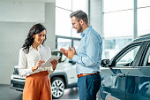 Cheerful car dealership customer talking to auto sales consultant
