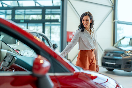 Businesswoman looking for a new car, standing next to a new SUV indoors at a car dealer