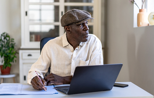 A male businessman is working at his laptop and writing documents in his office