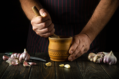 The chef crushes the garlic with a wooden pestle and mortar. We are preparing a national dish. Close-up of a chef's hands while working. Peasant products.