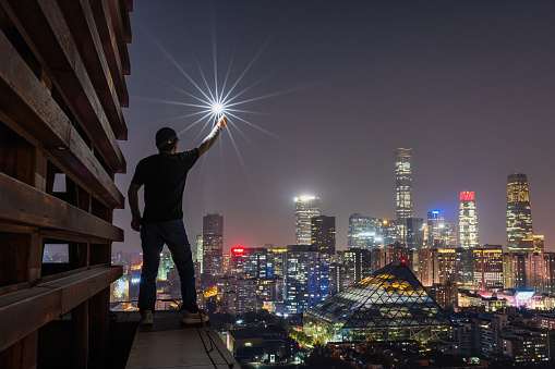 A photographer holding a light on the rooftop,The silhouette portrait at night in beijing cbd