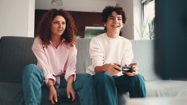 Mother and son playing video games while sitting on sofa at home
