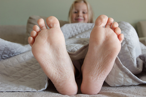 Feet under a light blanket on the bed, soft focus background. Concept of health