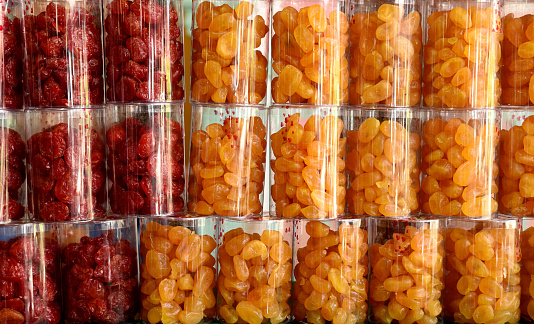 Closeup image of orange and red dried fruit products in clear plastic containers, stacked on top of each other.