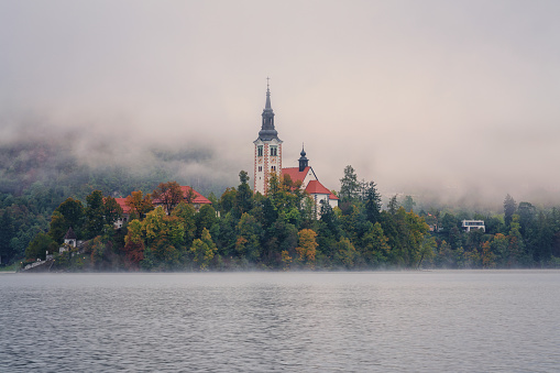 Famous alpine Bled lake (Blejsko jezero) in dense fog, amazing misty landscape, Slovenia. Scenic view of the lake, island with church and reflection in the water, outdoor travel background