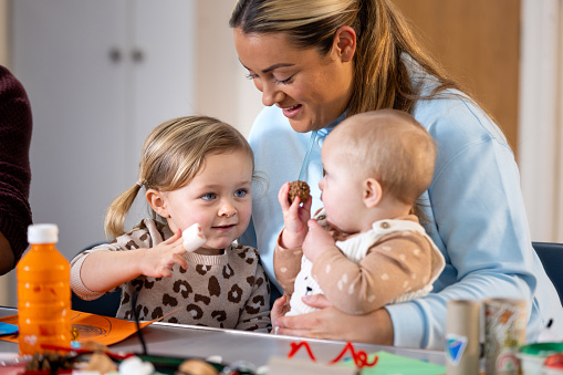 Close-up of a young adult with her two children on her lap at a baby class. The institute is located in Seghill, Northumberland.