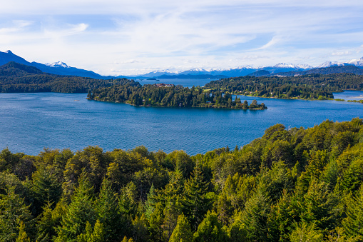 Nestled in the heart of Argentina, Bariloche unfolds as a picturesque haven, offering awe-inspiring views over the tranquil waters of its encompassing lake, with the majestic Andes serving as a grandiose backdrop. The pristine blue waters mirror the sky above, creating an expansive canvas that portrays nature's unadulterated beauty. The Andes, standing tall and resolute, frame this breathtaking scene, their snow-capped peaks whispering tales of ancient grandeur. This idyllic panorama encapsulates the serene yet profound essence of Bariloche, inviting onlookers to bask in the tranquility and timeless allure that is Argentina's natural splendor.