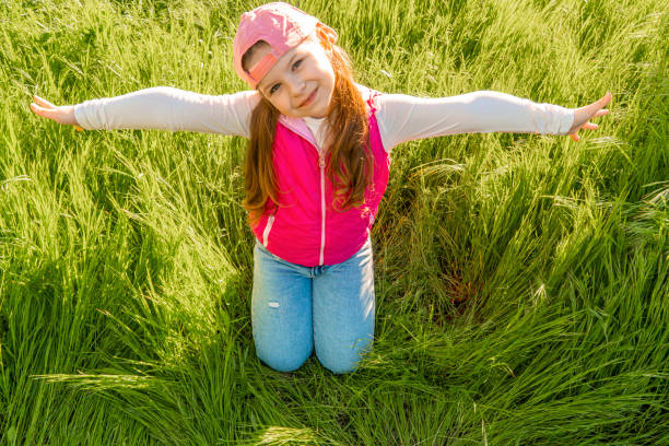 A cheerful girl sits in the thick green grass and spreads her arms to the sides. Walk outdoors in the city park