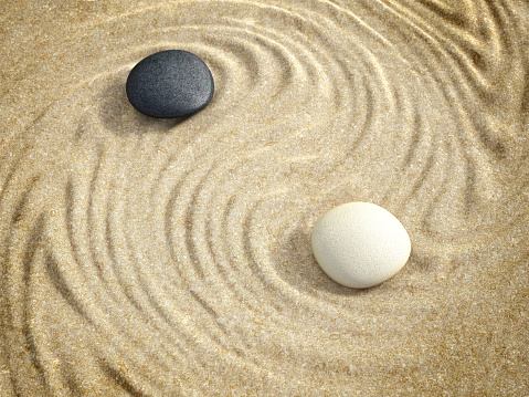Yin-Yang symbol formed with beach sands, black and white stones. Wellbeing concept.