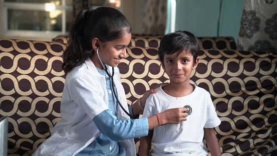 Happy child smiling while doctor is examining her lungs or heart during medical checkup in sunny office. Cheerful pediatrician using stethoscope to check respiration and heartbeat of her young patient