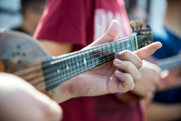 man wearing flat cap playing guitar leaning against fence.
