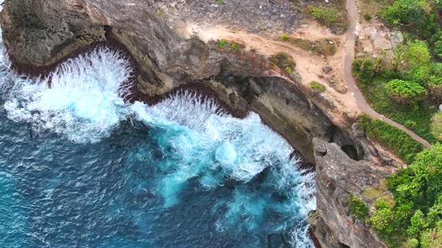 Aerial view closeup shot of waves crashing on the rocks along the coast at Nusa Penida island in Bali, Indonesia