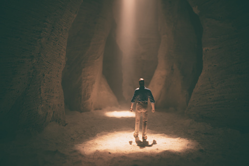 Here we see a silhouetted figure exploring a deserted slot canyon, with a thin beam of sunlight streaming through from overhead. Miniature photography.