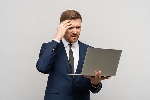 Businessman failed on stock exchange from decline in quotations, unsuccessful transaction. Tired upset sad trader man of problem in business, poor financial results looks at laptop on gray background