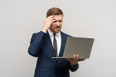 Man has problems in business, poor financial results looking at laptop on grey background.