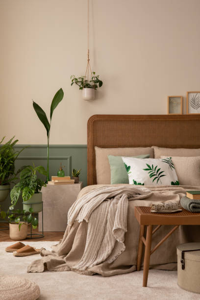 istock Warm and cozy bedroom interior with mock up poster frame, boho bed, beige bedding, green wall with stucco, books, brown slippers, plants in pots and personal accessories. Home decor. Template. 1731396859