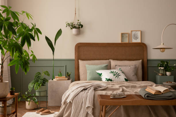 istock Warm and cozy bedroom interior with mock up poster frame, boho bed, beige bedding, green wall with stucco, books, brown slippers, plants in pots and personal accessories. Home decor. Template. 1731397533