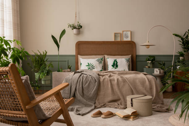 istock Warm and cozy bedroom interior with mock up poster frame, boho bed, beige bedding, green wall with stucco, books, brown slippers, plants in pots and personal accessories. Home decor. Template. 1731398148
