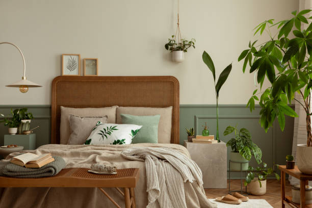 istock Warm and cozy bedroom interior with mock up poster frame, boho bed, beige bedding, green wall with stucco, books, brown slippers, plants in pots and personal accessories. Home decor. Template. 1731399305