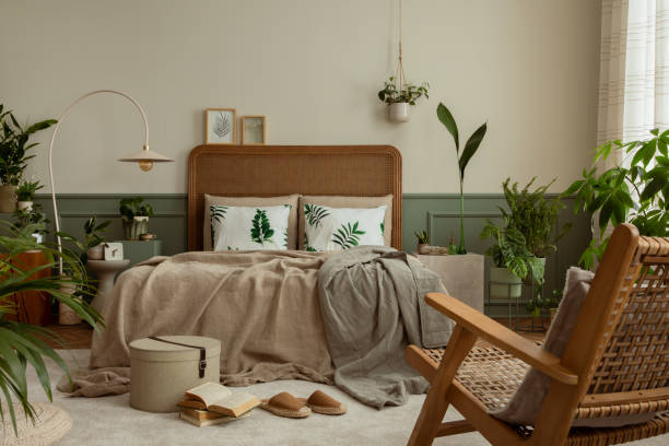 istock Warm and cozy bedroom interior with mock up poster frame, boho bed, beige bedding, green wall with stucco, books, brown slippers, plants in pots and personal accessories. Home decor. Template. 1731399321