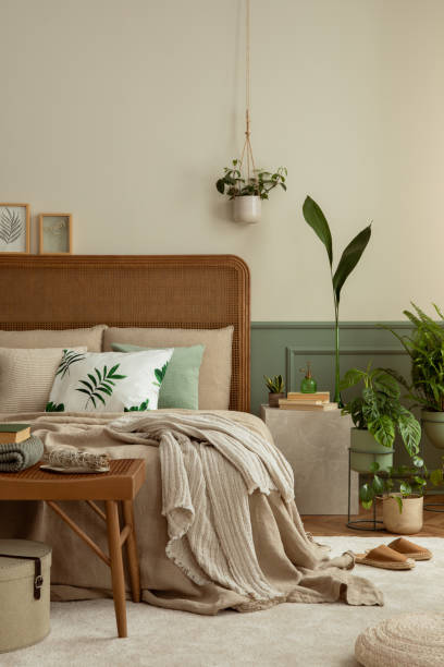 istock Warm and cozy bedroom interior with mock up poster frame, boho bed, beige bedding, green wall with stucco, books, brown slippers, plants in pots and personal accessories. Home decor. Template. 1731400897