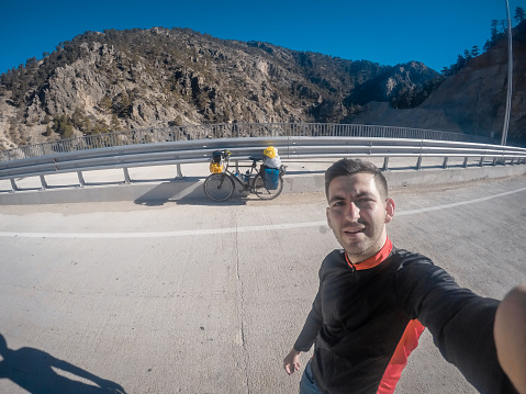 He is a 25-30 year old tour cyclist with a high spirit of adventure. He travels to different cultures and geographies by camping on his bike. He takes selfies with his own wide-angle camera. It is autumn season outdoors.