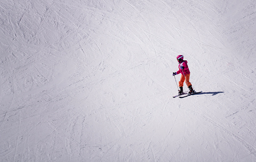 Queenstown, New Zealand - 23 Sep, 2023: At the remarkable ski resort, a woman gracefully skis downhill. Dressed in a vibrant pink jacket and orange pants, she stands out against the intricate snowy patterns.