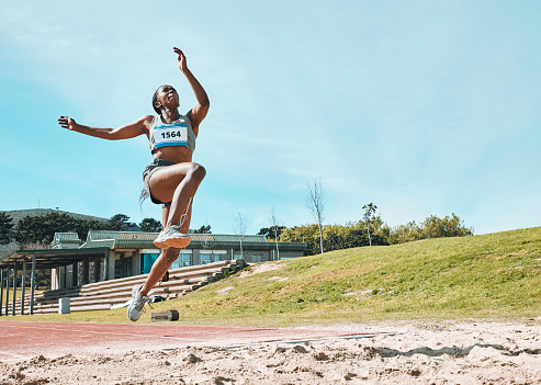Athletics, fitness and sports woman doing long jump in outdoor competition, athlete challenge or workout. Agility, sand pit and female person training, exercise and action performance at arena event