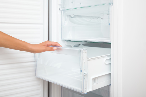 Young adult woman hand opening or closing plastic box of white freezer. Closeup. Side view.