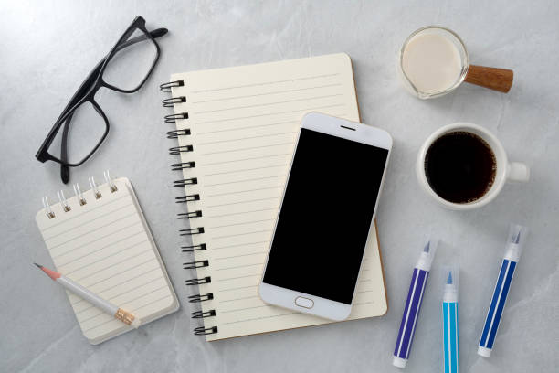 istock Mobile phone with blank mockup screen and book and coffee on stone texture background.Work desk. Top view. Flat lay. 1731453293
