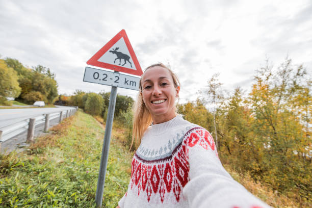 lustiges selfie einer frau, die mit einem warnschild für die elchkreuzung posiert - moose crossing sign stock-fotos und bilder
