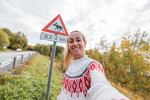 Funny selfie of woman posing with moose crossing warning sign
