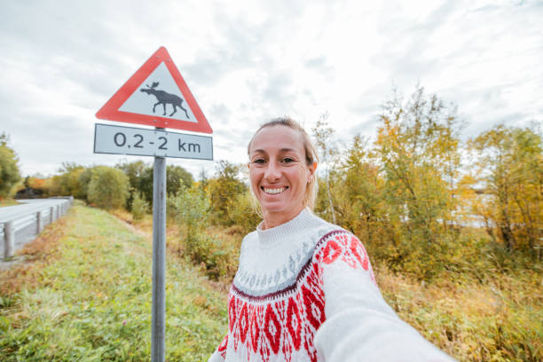 lustiges selfie einer frau, die mit einem warnschild für die elchkreuzung posiert - moose crossing sign stock-fotos und bilder