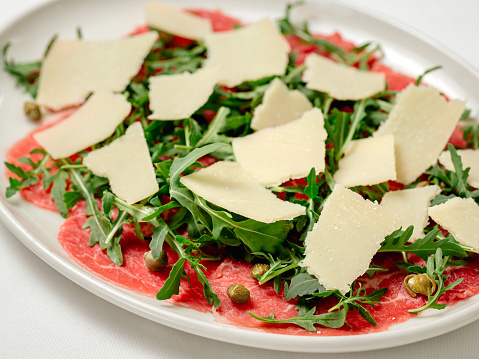 Beef Carpaccio cold appetizer with parmesan, capers and arugula on white plate extreme closeup view