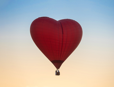 Hot Air Balloon in Red Heart Shape at sunset sky background. Evening hot-air balloon flight with beautiful sunlight. Romance of ballooning in good weather