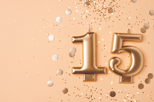 Gold candles in the form of number fifteen on peach background with confetti. 15 years celebration.