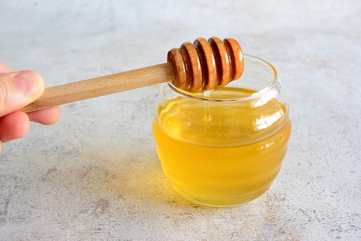 jar with transparent honey and honey dipper in the hand