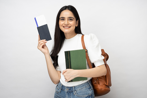 Portrait of young women student showing plane ticket and passport standing isolated over white background