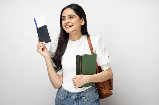 Portrait of young women student showing plane ticket and passport standing isolated over white background