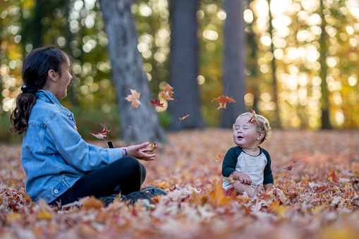 A sibling duo play in the leaves on a warm fall day, during a family camping trip.  They are tossing them up into the air as they watch them fall and laugh with joy.