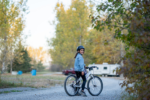 A young girl is seen on her bike as she tours around the campground during a family trip.  She is dressed warmly in fall layers and has a helmet on for safety.