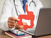 Treatment and prevention of constipation and diarrhea. Close-up of hand doctor holding a large intestine symbol made from paper while sitting at the table