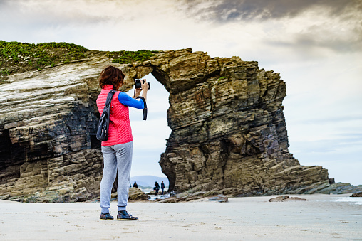 Tourist woman taking travel photo from cliff formations on Cathedral Beach in Galicia Spain. Playa de las Catedrales, As Catedrais in Ribadeo, province of Lugo, northern Spain.