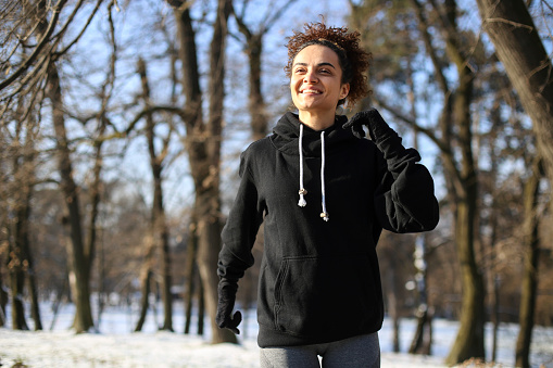 Young woman running in nature during winter. About 25 years old mixed-race female.