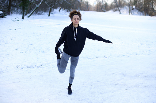 Young woman warming up exercising in nature during winter. About 25 years old mixed-race female.
