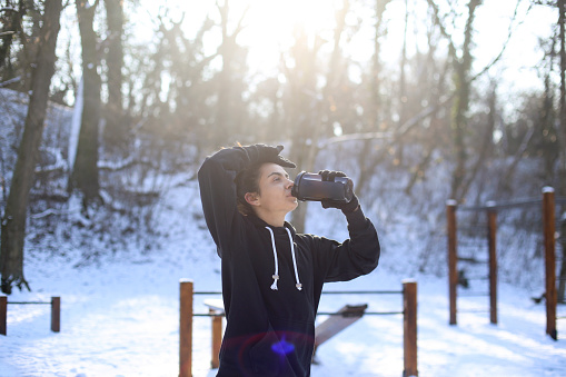 Young woman taking a break after an exercise in nature during winter. About 25 years old mixed-race female.