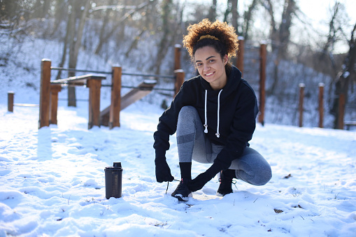 Young woman preparing to exercise in nature during winter. About 25 years old mixed-race female.