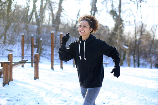 Young woman running in nature during winter. About 25 years old mixed-race female.