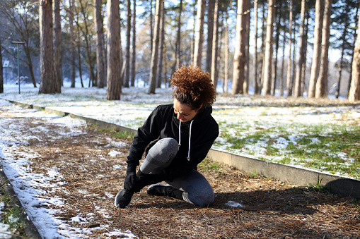 Young woman injured during running in nature during winter. About 25 years old mixed-race female.