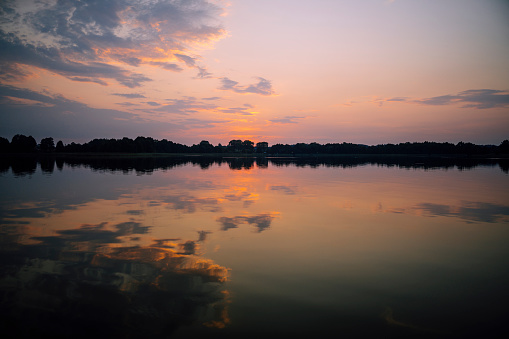 Orange sun setting over beautiful scenery of lake and distant forest